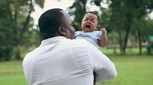 An African-American father lovingly holds a crying baby. A young black man soothing a crying infant. Family Concept.
