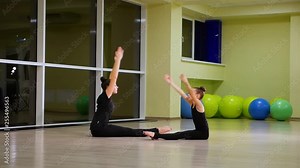Two slim cute girls sisters artistic gymnasts in black sportswear make warm-up in gym and perform muscle stretching exercise. Rhythmic gymnastics for child and teenager.