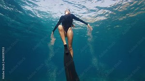Woman freediver ascends. Young female freediver swims underwater and plays with sand making sandy traces underwater