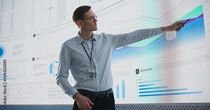 Male CEO Of Data Science Company Is Giving Presentation In Front Of Big Digital Screen With Graphs And Charts. Successful Caucasian Man Reviewing Business Accomplishments And Objectives In the Office.