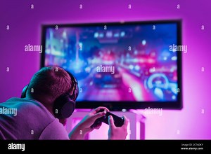 Back view shot of professional gamer playing online video game on his gameset. Room lit in neon light and retro style. Using headphones to talk with the team. Entertainment, fun concept Stock Photo - Alamy