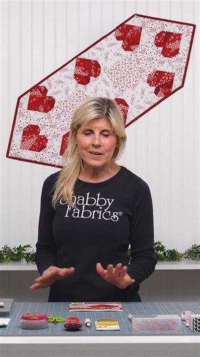 Create a heartwarming piece for your home with the Foundation Paper Piecing Hearts Table Runner, designed by Shabby Fabrics and colored with the Redberry Lane collection by Henry Glass Fabrics. Red paper pieced hearts line the border of this dynamic runner that tapers to two elegant points. Contrasted with crisp white prints that feature houses and flowers, this project is great for adding a sentimental touch to a space. | Shabby Fabrics