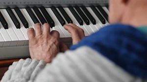 a pensioner in a dressing gown plays the piano while being at home. an elderly man practices playing a musical instrument, an elderly man's hobby is playing the synthesizer