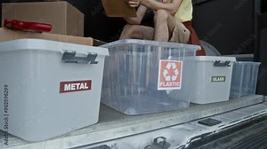 Medium close-up shot of hands of unrecognizable female volunteer placing label on container for sorting rubbish, while preparing for public ecology event in local park