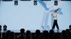 Caucasian woman female speaker presenting on the stage during ecological renewable energy conference. Future technology meetup. Talks about green energy sources, wind turbines, solar power