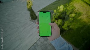 View on hands holding and scrolling vertically phone with green screen. On background stairs outdoors. Nature
