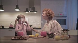 young, beautiful mother and daughter drink tea with cookies in the kitchen. A young family in a beautiful large kitchen eats cookies and drinks tea.