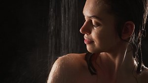 Attractive lady taking a shower with pleasure isolated over black background in slowmotion