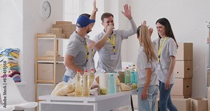 Team of volunteers stands in a circle, exchanging high fives before work of packing food into boxes for donation. Their collaborative spirit and unity reflect the essence of teamwork and charity.