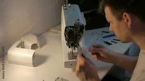 Young repairman master is repairing sewing machine sitting at table, side view. Unscrew body of sewing machine using screwdriver. Man is testing and disassembles the sewing machine.