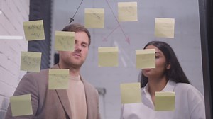 Businessman And Businesswoman Brainstorming With Sticky Notes On Glass Window | Free Stock Video Footage