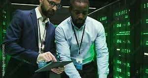 Mixed-races men checking program and working on tablet device and laptop computer. Software engineers analyzing big data of storage. Multiethnic males analytics in data center. Digital security.