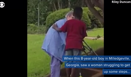 Boy helps elderly woman struggling to walk up stairs