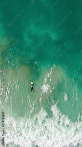 Vertical Screen: Witness a lone surfer expertly riding the waves in beautifully clear ocean waters in this mesmerizing aerial footage showcasing skilled surfing in natures stunning setting