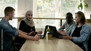 Diverse people using laptops while sitting at bright work place in front the window, multi-ethnic and multi cultural young people working as team, discussing start-up. Overview, accelerating footage