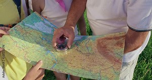 Above view of group of tourists with guide looking on map, planning hiking in mountains. Crop view of male guide hands with kids checking route on map, using compass at campsite. Concept of hiking.