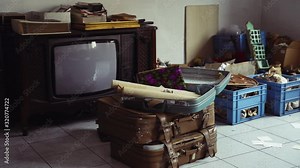 Retro style room with pile of antiques on the floor. Old TV, vintage suitcases for travel and dispersed ancient photos from family album. Nostalgia and memory, way of life, retro dump in the room