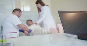 Young, ill patient lying on a bed at the hospital. Female doctor examining his breathing using stethoscope while male doctor is preparing him for an infusion for faster recovery.