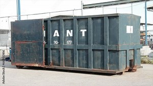 blue container large rental temporary mobile transport dumpster bin with doors open outside in summer on cement pavement in summer with a fence behind