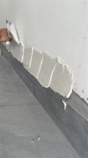worker applying thick plaster or putty to the joint between wall and floor