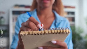 Closeup of hand African American woman with pen making notes in notepad making shopping list or fixing work schedule and plan of work meetings so as not to forget anything standing in office room
