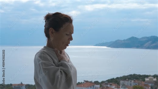 Woman using asthma inhaler during allergic attack outdoors. Mature woman experiencing shortness of breath from an asthma attack and using an aerosol inhaler for relief, with a sea and mountain view