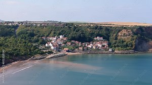 Aerial footage of Runswick Bay, a scenic village in North Yorkshire with cliffs, ocean and a sandy beach with cottages and countryside