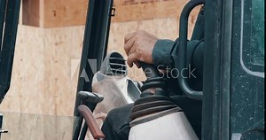 Construction worker in front loader machine controlling joysticks on work site
