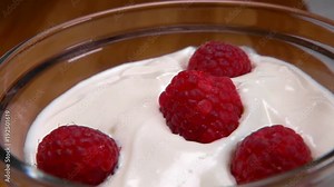 Raspberry falls in a glass bowl of yogurt in slow motion