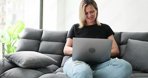 Woman smiles, sits on sofa participates in remote webinar. Freelancer doing remote work or having fun online