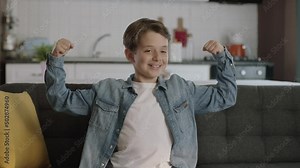 Little boy shows his arm muscles to the camera.Portrait of little boy showing biceps, muscles, strength to camera at home.Superhero kids game.