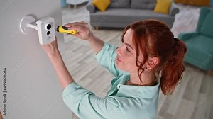 installing surveillance camera in house, young woman with screwdriver mounting wireless cam on wall for home security system
