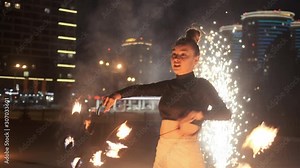 Exotic female asian dancer moves with flaming torches. Sparks burning stream on the background. Rush of light and fire. Spectacular authentic street show with fire.