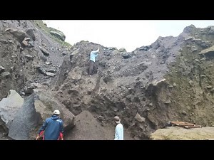 One person mines black sand from a cliff, two miners separate the rocks and sand below.