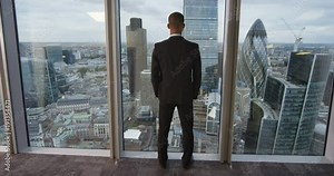 4K View from behind of young successful business executive looking out at view of the city. View from the window shows famous London skyline with iconic buildings. Slow motion.