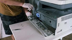 printer repair technician. A male handyman inspects a printer before starting repairs at the service center.