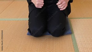 和室で座布団の上に正座で座るスーツ姿の男性