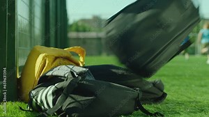 Kids throwing their backpacks on the grass ground and running to play football after school lessons . Close up many bags or schoolbags on the floor . Children playing soccer on background in sunny day