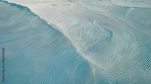 A birdseye perspective of rippling textures and patterns on the surface of the salt flats glistening in the sun.