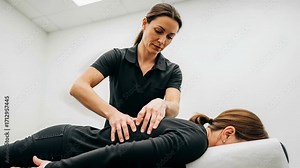 Manual therapist performs spinal adjustment on a patient to improve posture and relieve tension in a clinical setting