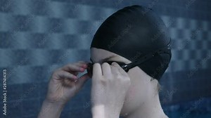 Young girl putting on swimming goggles in an indoor swimming pool before training