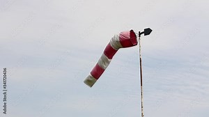 Windsock, red and white pointer is indicating strength and direction of the wind against cloudy sky.