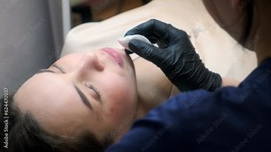 Microblading lip tattoo with a special coloring pigment that corrects the color of the lips in a cosmetology clinic. Hand doing lip cleaning procedure with cotton pad