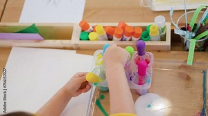 Little Child Drip Painting Holding Dropper and Sucks in Colored Water into Pipette From Containers - Hands Close-up. Child Study Drawing Watercolors - Top View