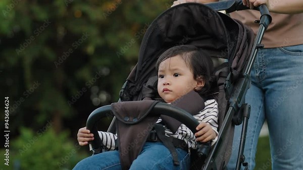 mother pushing toddler baby stroller and walking in the park