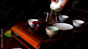 Chinese tea ceremony. Close up of hand take the teapot and pouring the hot tea into the glass serving jar with ceramic tea cup set on the table.