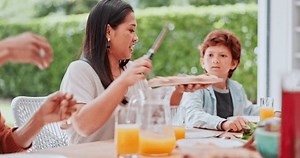 Family, serve and food at table for lunch, party or event with unity, bonding and conversation in home. People, pizza and knife with beverage or support with dinner, nutrition and meal in dining room