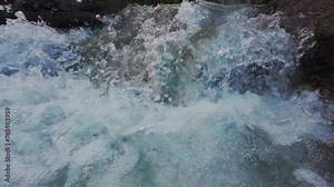 Lively and splashing flow of a small mountain stream. Fresh spring water making its way between mossy and snow covered rocks. Slow motion.