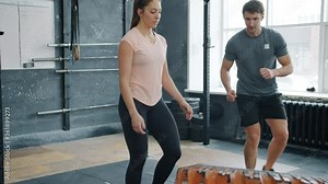 Slow motion of muscular girl lifting heavy tyre in gym working with crossfit trainer focused on weightlifting exercise. People and bodybuilding concept.