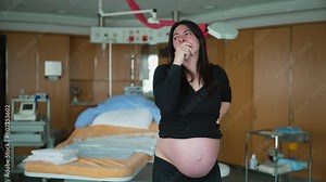 Pregnant woman having contractions standing at clinic with hospital equipment in background struggling with pain, real life authentic 30s lady before childbirth pre labor